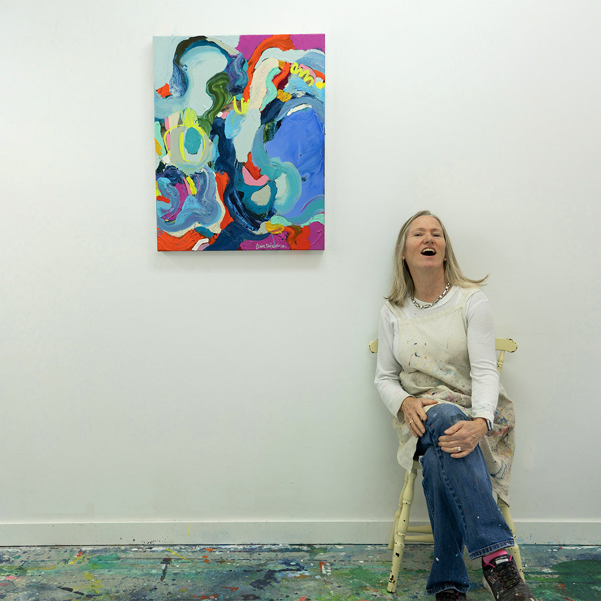 Abstract painting, No Such this As Luck, hung on white studio wall, artist Claire Desjardins sat on a chair to the the right for scale.